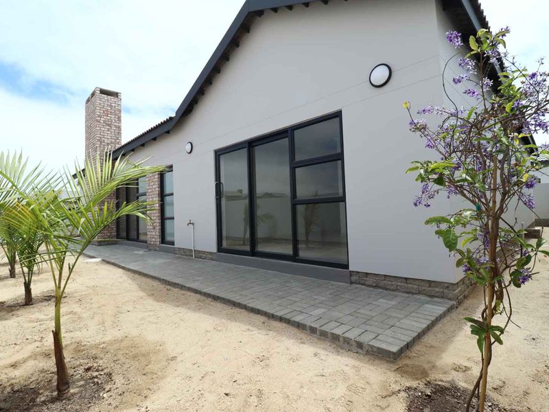 Rear view of the property featuring a paved patio, brick chimney, and modern sliding glass doors leading into the home.