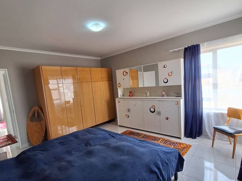 A bedroom featuring tiled flooring, built-in wooden cupboards, and a large window allowing natural light.
