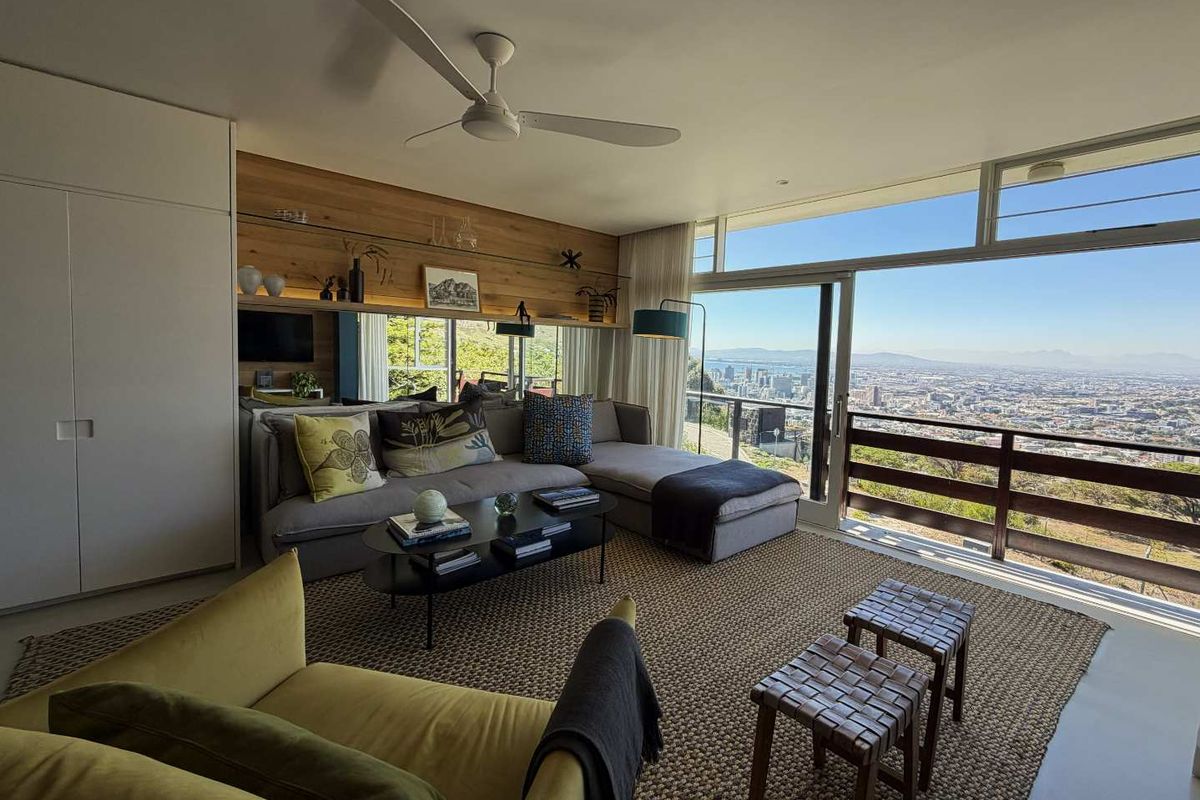 Modern living room featuring a wood-paneled feature wall, ceiling fan, and large sliding glass doors opening to a balcony with expansive city views.