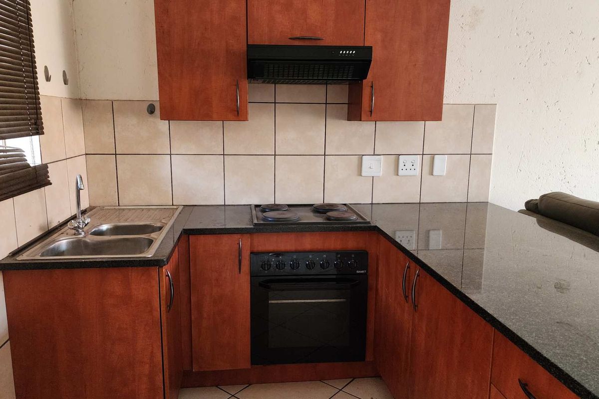 Compact kitchen featuring cherry-wood cabinetry, granite countertops, a built-in oven, electric hob, extractor fan, and a double-basin stainless steel sink.