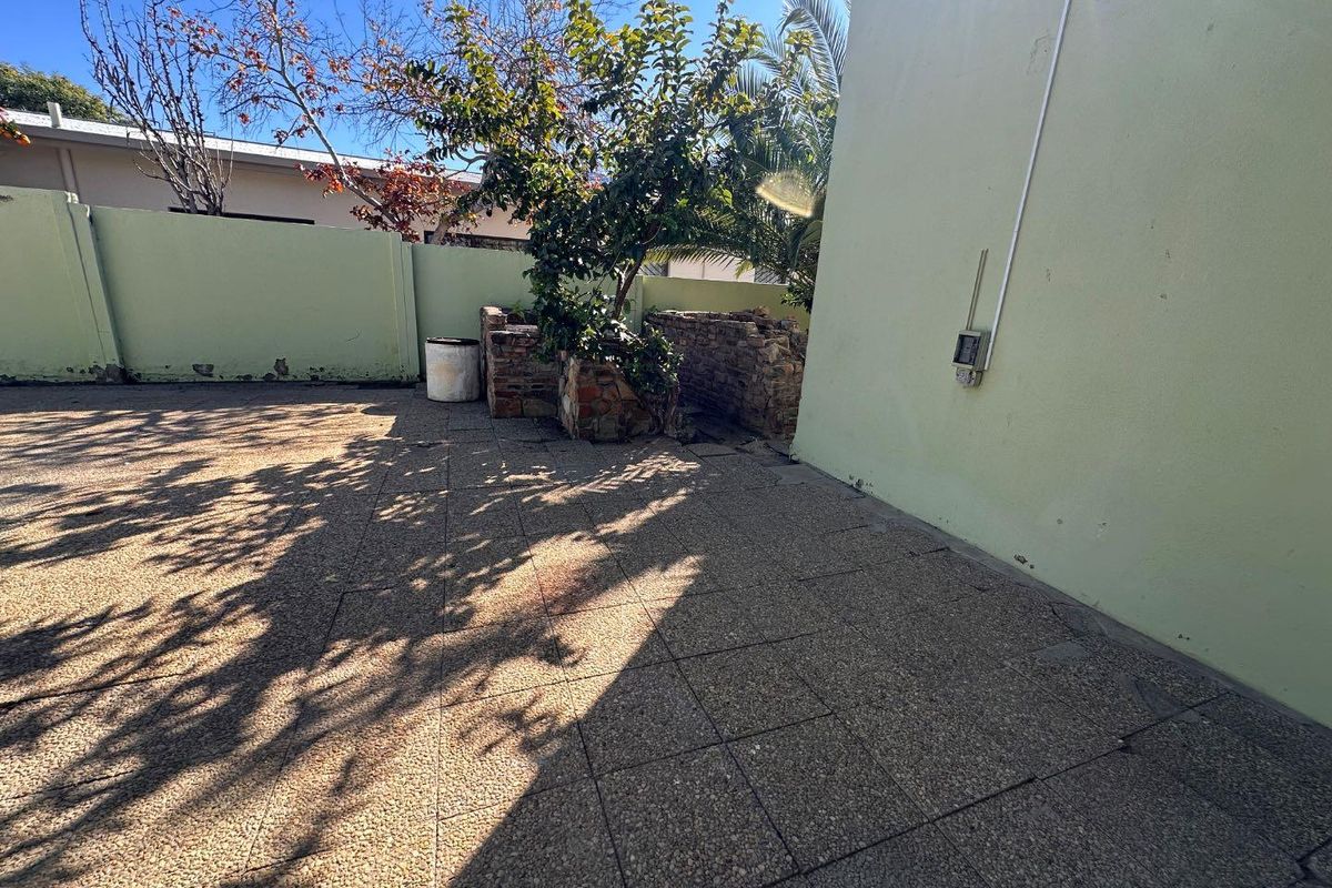 A paved rear courtyard area featuring a stone planter and boundary walls requiring maintenance.