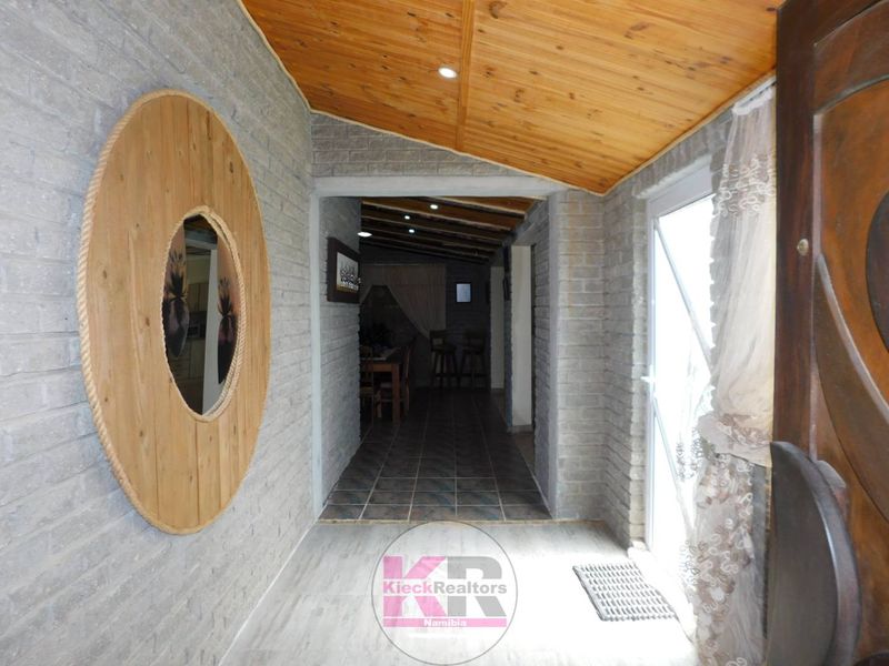 Welcoming entrance hall featuring exposed brick walls, a warm timber-clad raked ceiling with recessed lighting, and durable tiled flooring leading into the home.