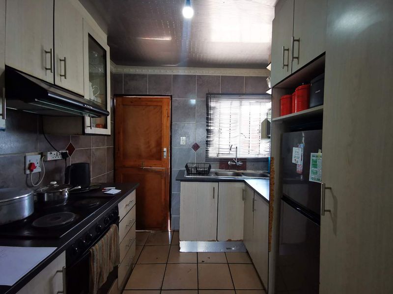 A compact kitchen featuring built-in cabinetry, a double sink, tiled backsplash, and integrated cooking appliances, showing signs of wear and tear.