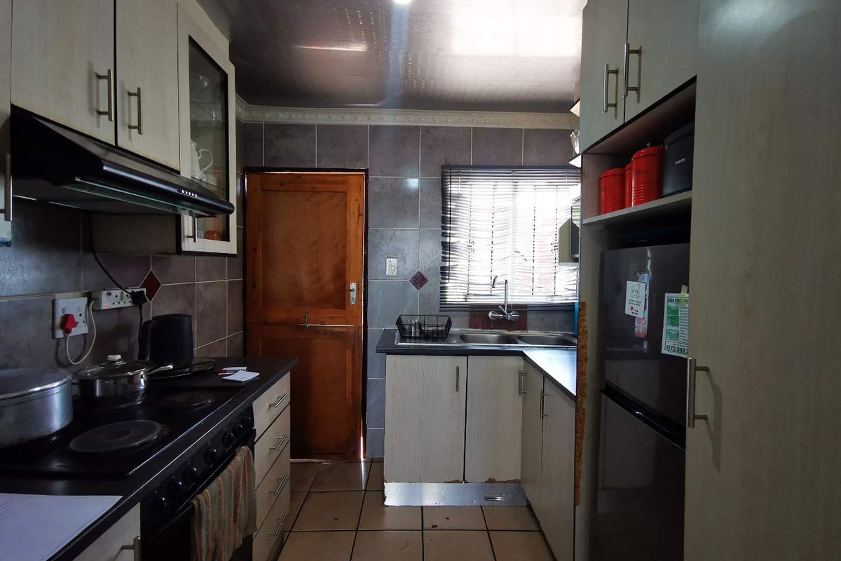 A compact kitchen featuring built-in cabinetry, a double sink, tiled backsplash, and integrated cooking appliances, showing signs of wear and tear.