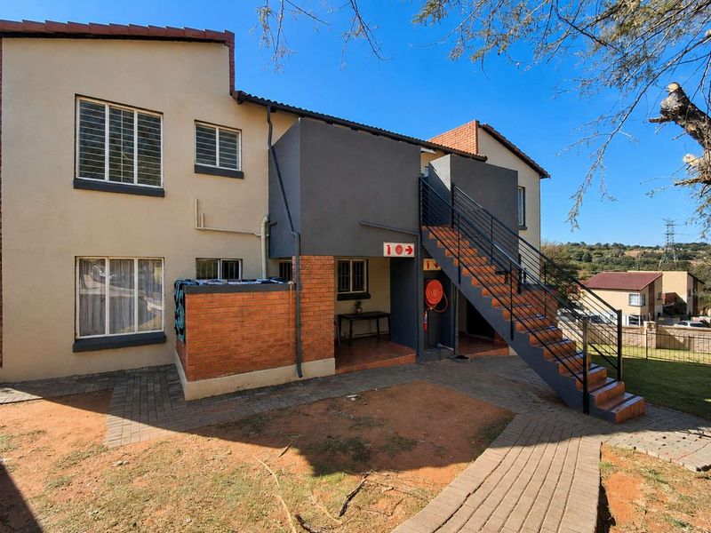 Rear view of the apartment building featuring an external staircase, paved walkways, and a covered patio area with fire safety equipment.