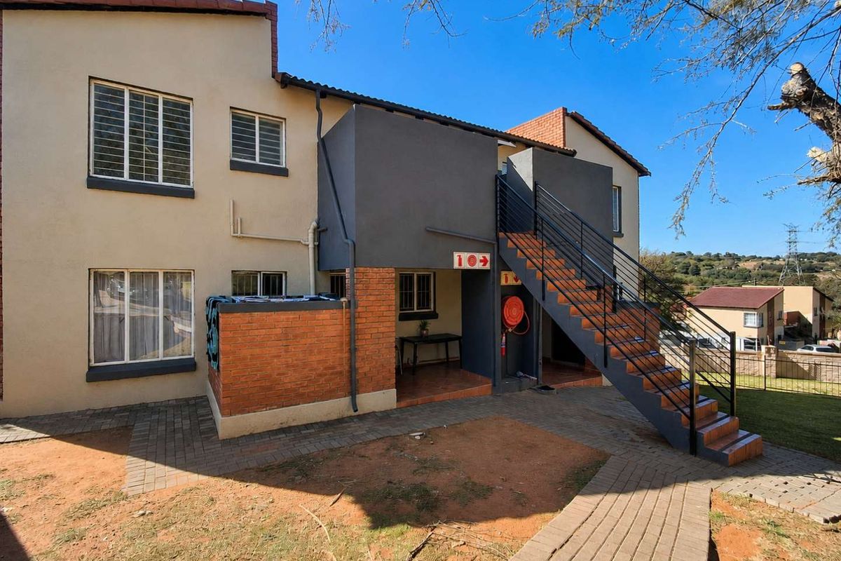Rear view of the apartment building featuring an external staircase, paved walkways, and a covered patio area with fire safety equipment.