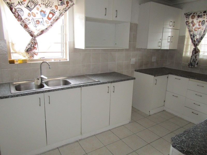A functional kitchen featuring white built-in cabinetry, laminate countertops, a stainless steel double sink, and neutral tiled flooring and backsplash.