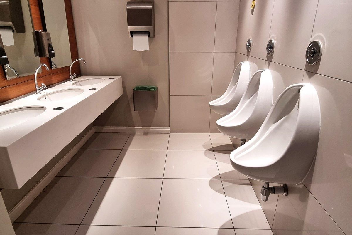 A clean, modern commercial bathroom featuring a row of wall-mounted urinals and a sleek integrated vanity with multiple basins.