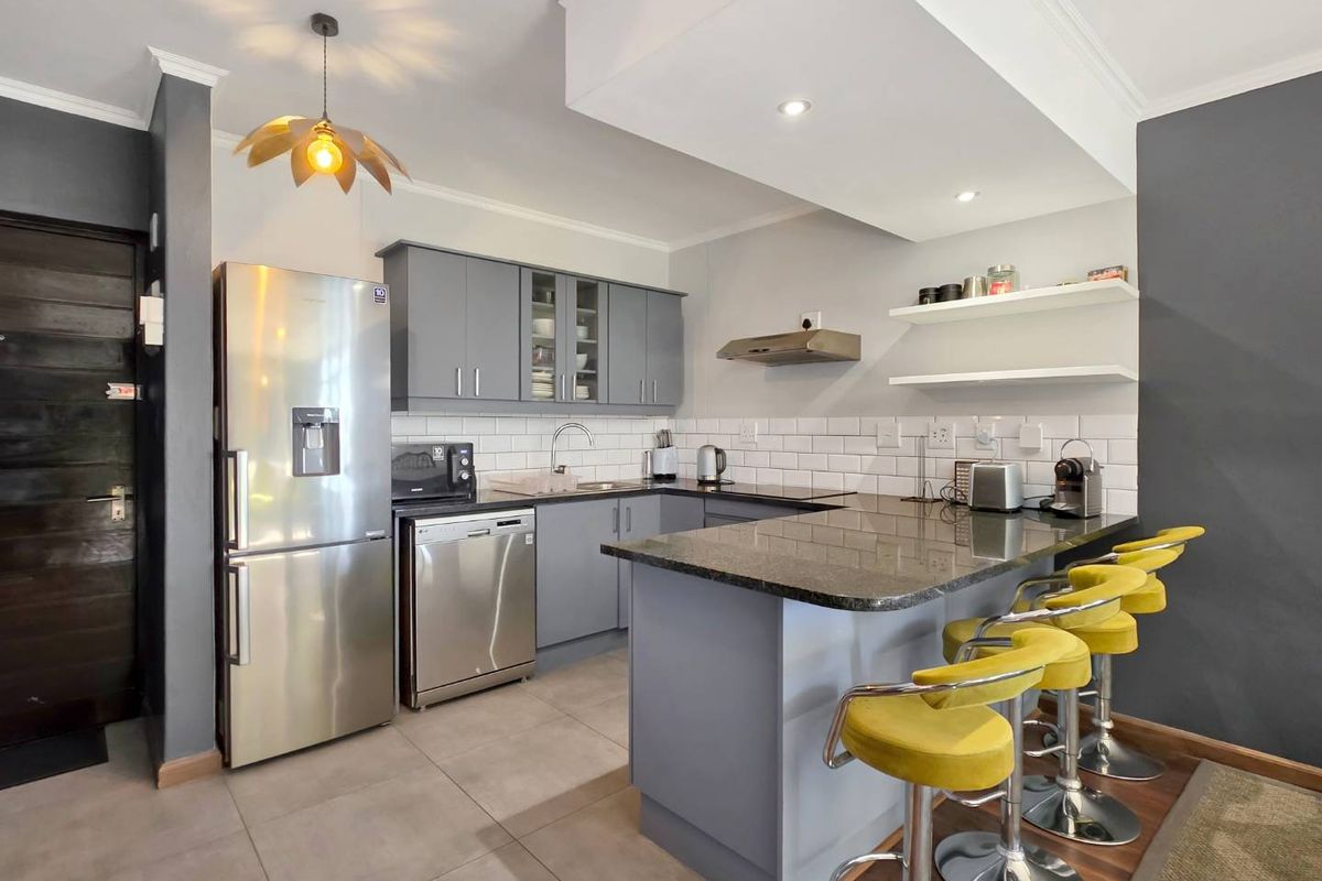 Modern kitchen featuring grey cabinetry, granite countertops, subway tile backsplash, and a breakfast bar with integrated lighting.