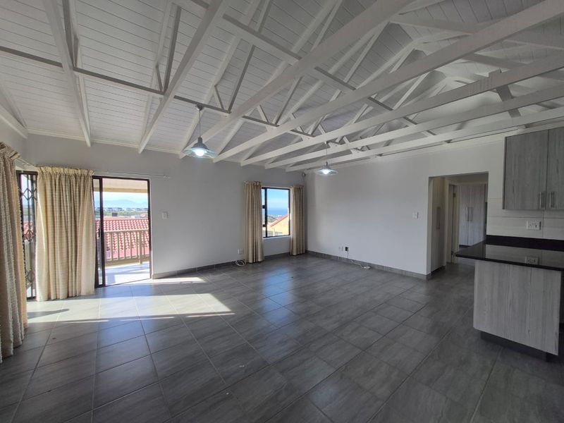 Spacious open-plan living area featuring high exposed timber truss ceilings, tiled flooring, and direct access to a balcony with scenic views.