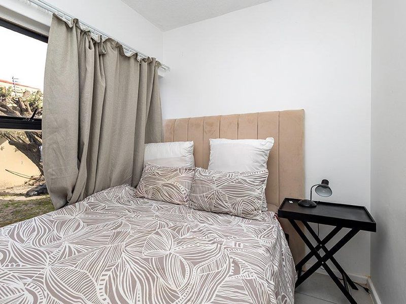A compact bedroom featuring a large aluminium-framed window with views of the exterior area.