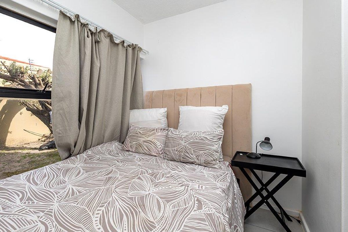 A compact bedroom featuring a large aluminium-framed window with views of the exterior area.