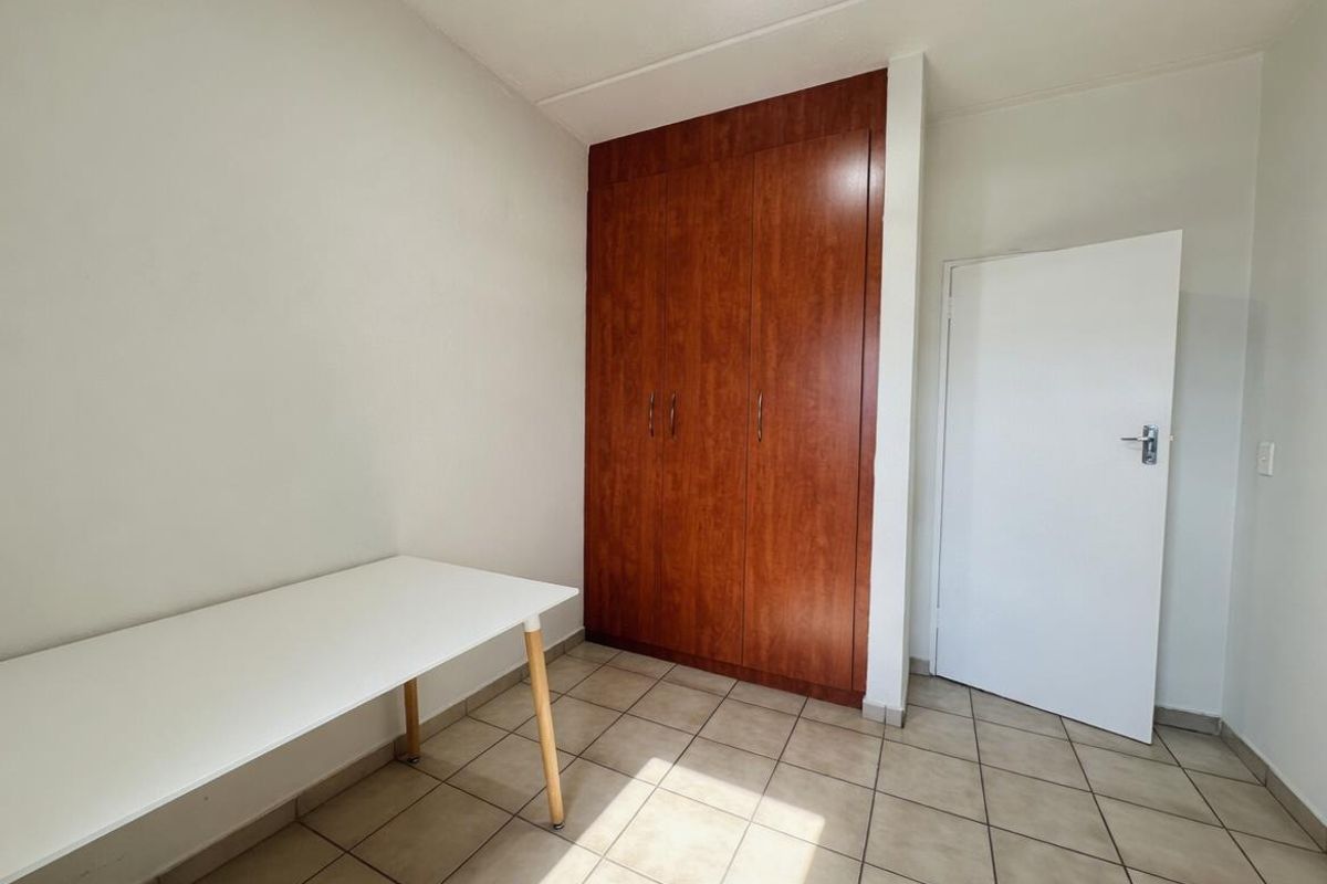 A bedroom featuring tiled flooring and a built-in wooden wardrobe, providing functional storage space.