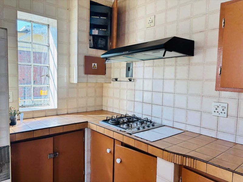 A dated kitchen featuring tiled countertops, built-in cabinetry, a gas hob, and an extractor fan, with an exposed electrical distribution board.