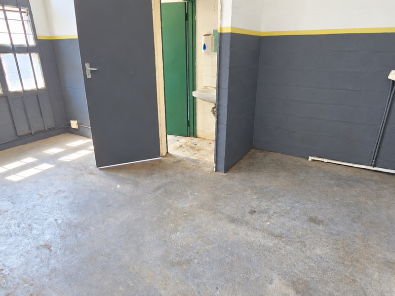 A functional industrial utility space featuring exposed concrete floors, painted masonry walls, steel-framed windows, and a small integrated wash basin.