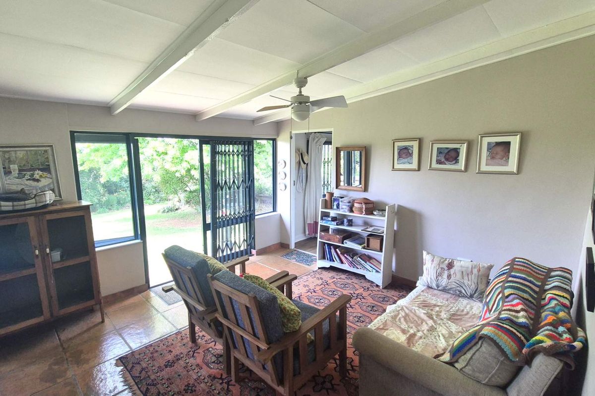 A cozy living room featuring tiled flooring, exposed ceiling beams, a ceiling fan, and a sliding glass door providing access to the garden.