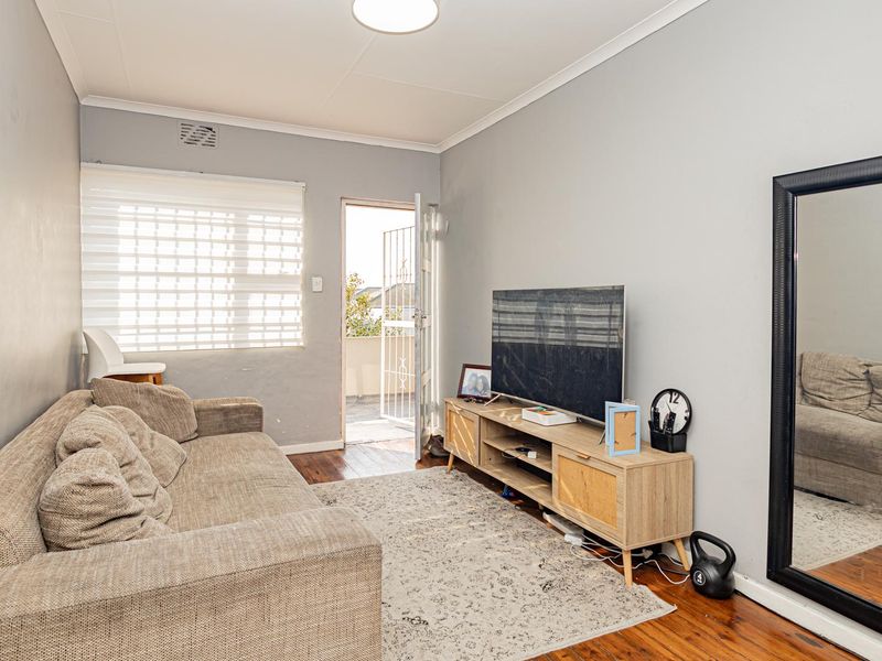 A living room featuring timber flooring, neutral wall tones, and direct access to an outdoor balcony area through a security gate.