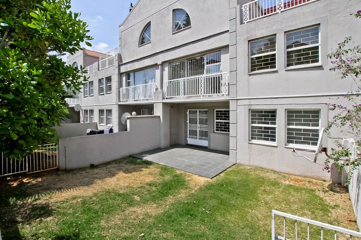 Rear view of the townhouse featuring a small tiled patio, private garden area, and upper-level balconies with security features.
