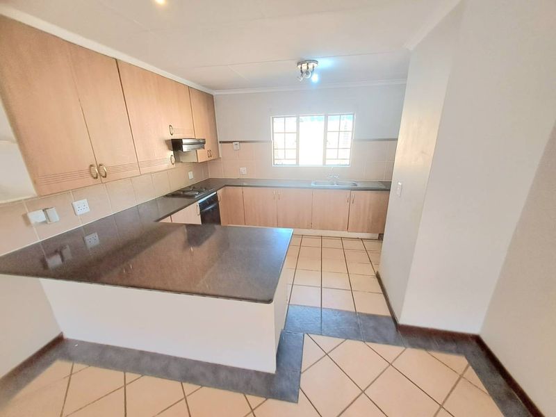 A functional kitchen featuring laminate cabinetry, stone countertops, built-in oven, hob, extractor fan, and tiled flooring in an open-plan layout.