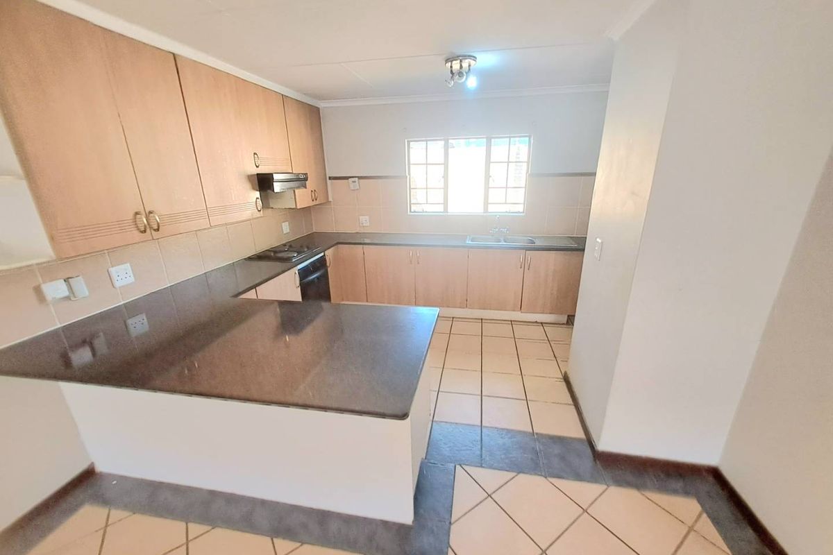 A functional kitchen featuring laminate cabinetry, stone countertops, built-in oven, hob, extractor fan, and tiled flooring in an open-plan layout.