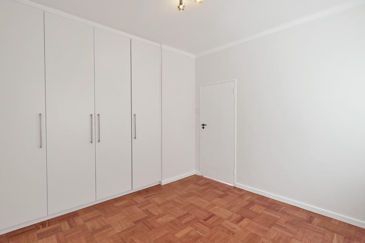 A bright, empty bedroom featuring well-maintained parquet flooring and floor-to-ceiling built-in cupboards.