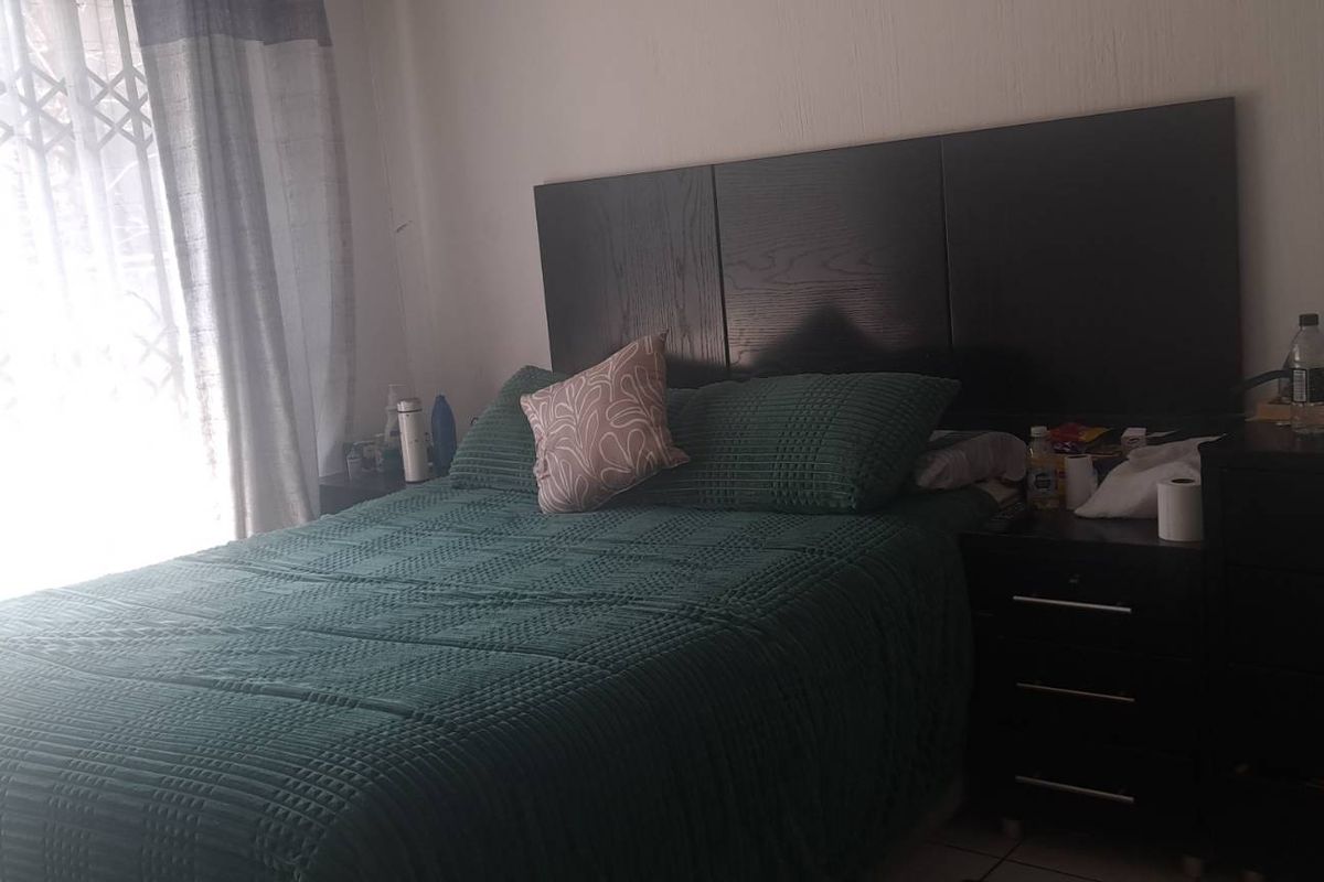 A standard bedroom featuring tiled flooring and a security gate over the window, providing basic natural light and access to the exterior.