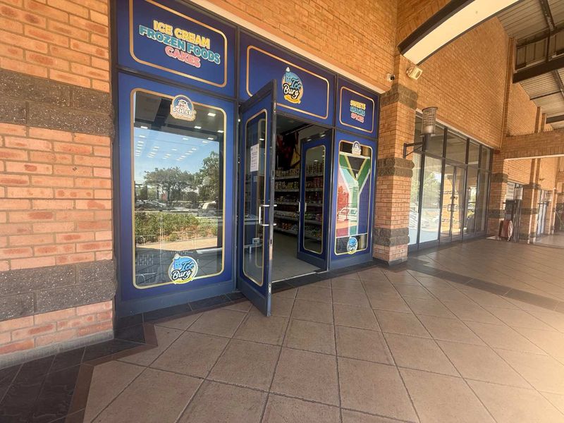 Front entrance of a commercial retail unit featuring a brick facade, large glass storefront, and tiled walkway.
