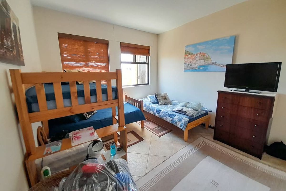 A functional bedroom featuring tiled flooring and two windows with fitted bamboo blinds, providing natural light and a practical layout.