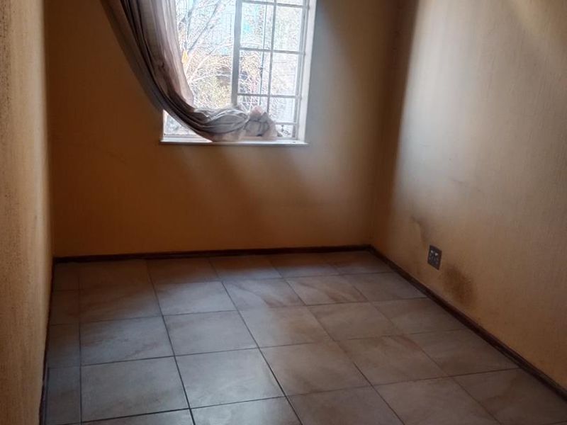 An empty bedroom featuring tiled flooring and a window with security bars, requiring cosmetic updates to the wall finishes.