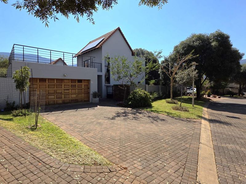 Front exterior view of a modern house featuring a paved driveway, wooden garage door, and an upper-level balcony with metal railings.