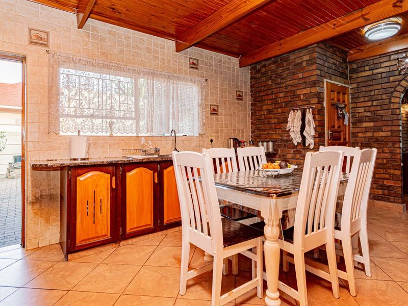 Open-plan living and kitchen area featuring exposed timber ceiling beams, a rustic brick feature wall, tiled flooring, and built-in cabinetry with granite countertops.
