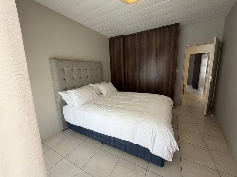 A well-maintained bedroom featuring built-in wooden cupboards, neutral tiled flooring, and a clean panelled ceiling, offering a functional and comfortable living space.
