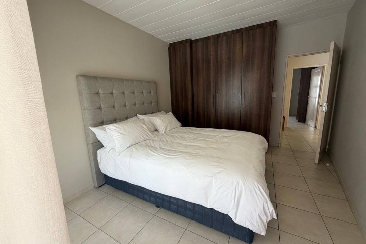 A well-maintained bedroom featuring built-in wooden cupboards, neutral tiled flooring, and a clean panelled ceiling, offering a functional and comfortable living space.