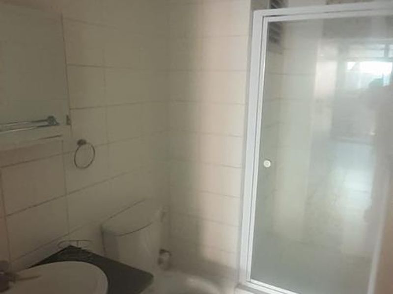 A functional bathroom featuring a vanity cabinet, toilet, and a glass-enclosed shower with tiled finishes throughout.