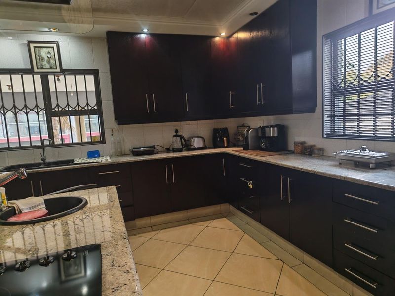 A well-maintained kitchen featuring dark wood cabinetry, granite countertops, a built-in hob, and tiled flooring with ample storage space.