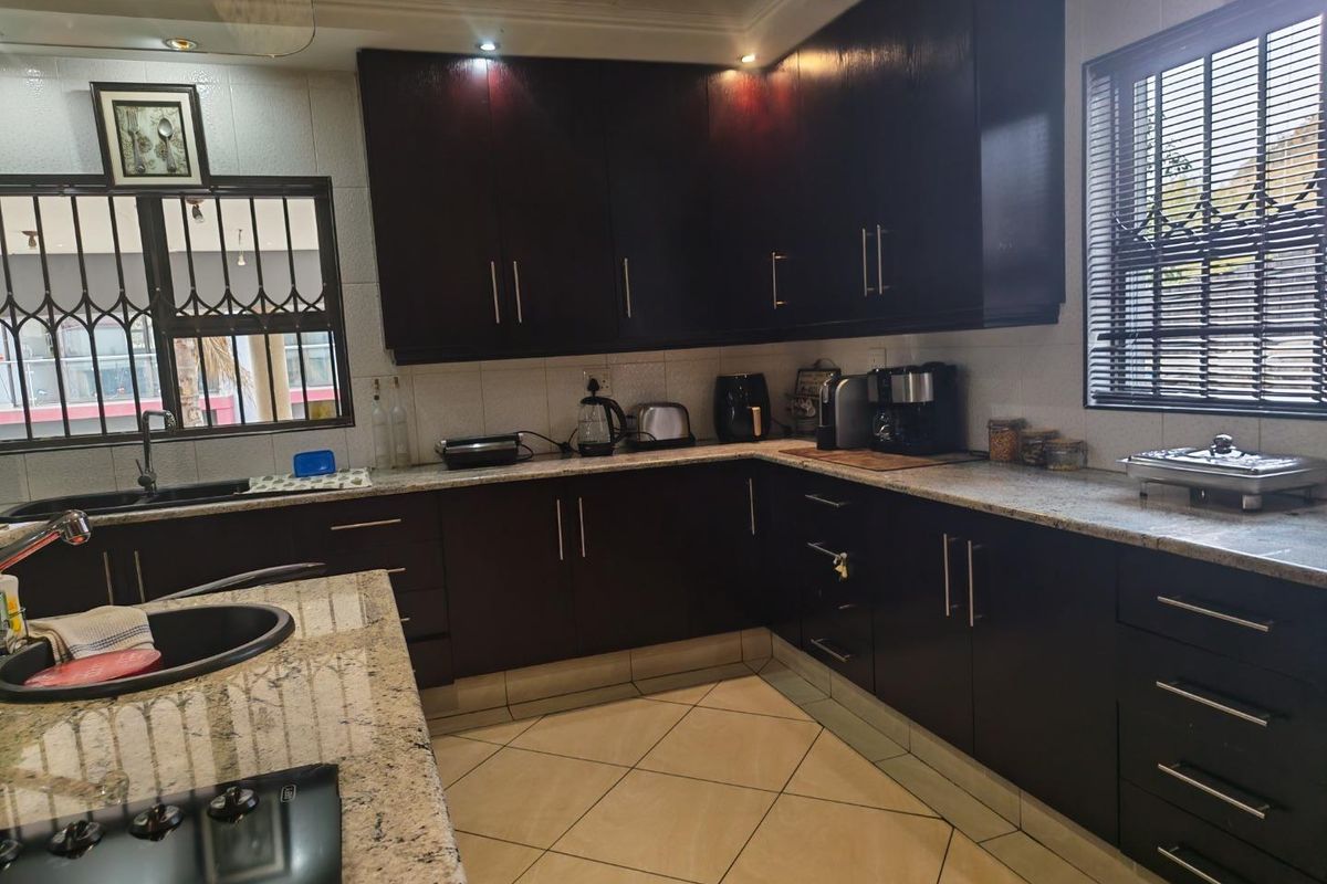 A well-maintained kitchen featuring dark wood cabinetry, granite countertops, a built-in hob, and tiled flooring with ample storage space.