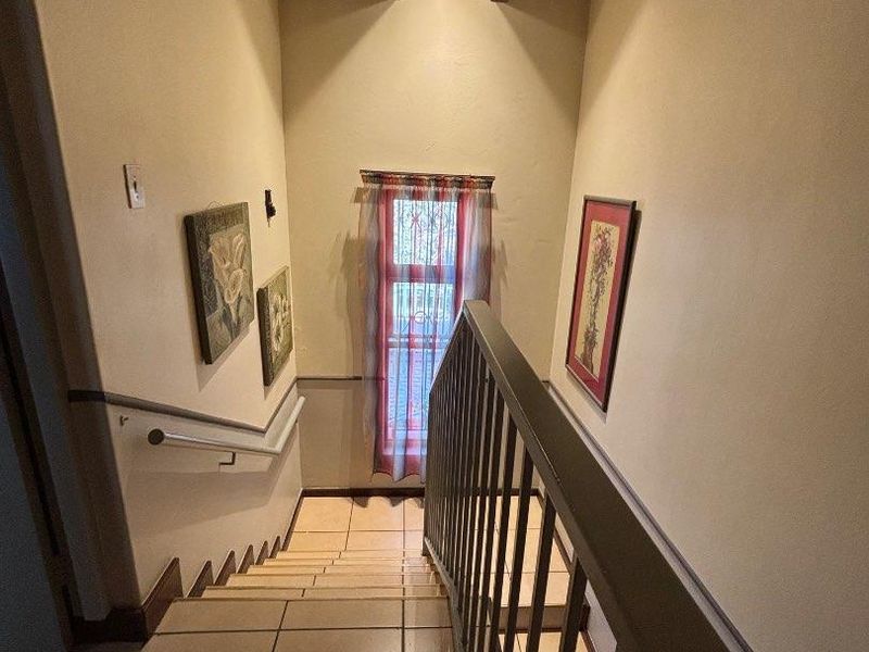 A staircase hallway featuring tiled steps, a metal balustrade, and exposed timber ceiling beams, providing access between levels.
