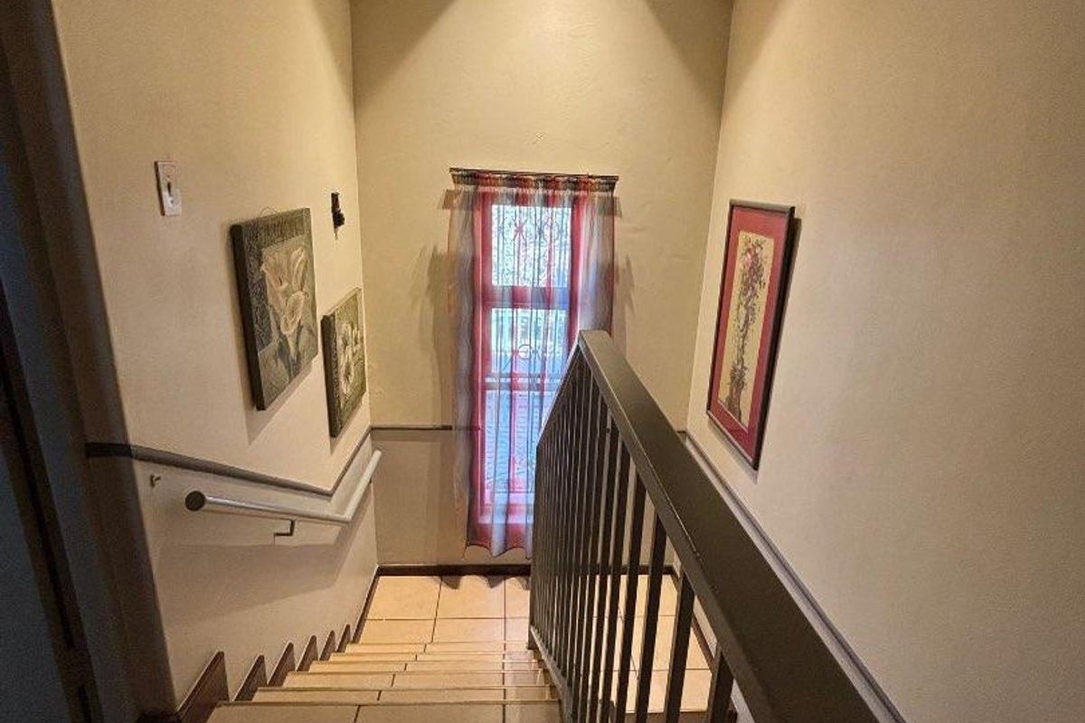 A staircase hallway featuring tiled steps, a metal balustrade, and exposed timber ceiling beams, providing access between levels.