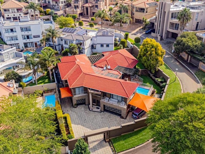Aerial view of a residential property featuring a tiled roof, paved driveway, swimming pool, and secure boundary walls within a suburban estate.