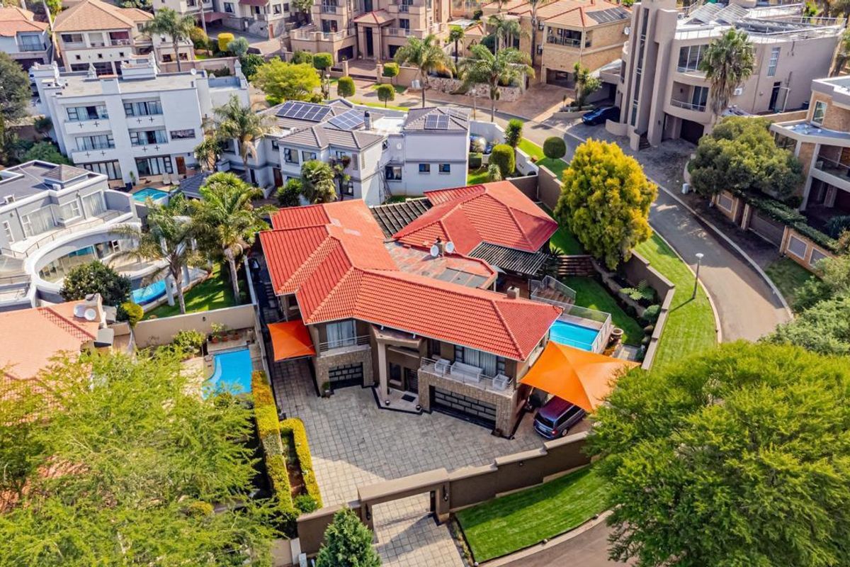 Aerial view of a residential property featuring a tiled roof, paved driveway, swimming pool, and secure boundary walls within a suburban estate.