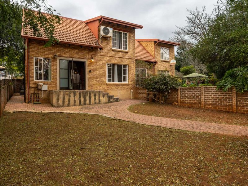Rear view of a face brick townhouse featuring a paved patio area, garden space, and secure brick boundary walls.