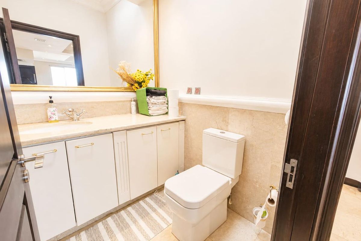 A well-maintained bathroom featuring a stone-topped vanity cabinet, undermount sink, large wall mirror, and modern toilet with neutral stone wall and floor tiling.