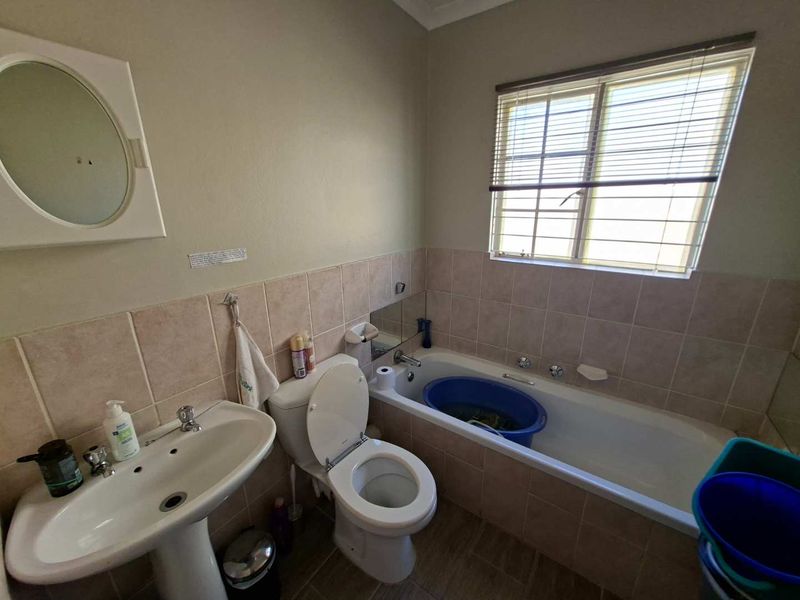 A functional bathroom featuring a pedestal basin, toilet, and a bathtub with tiled splashback, offering a practical layout with natural light.