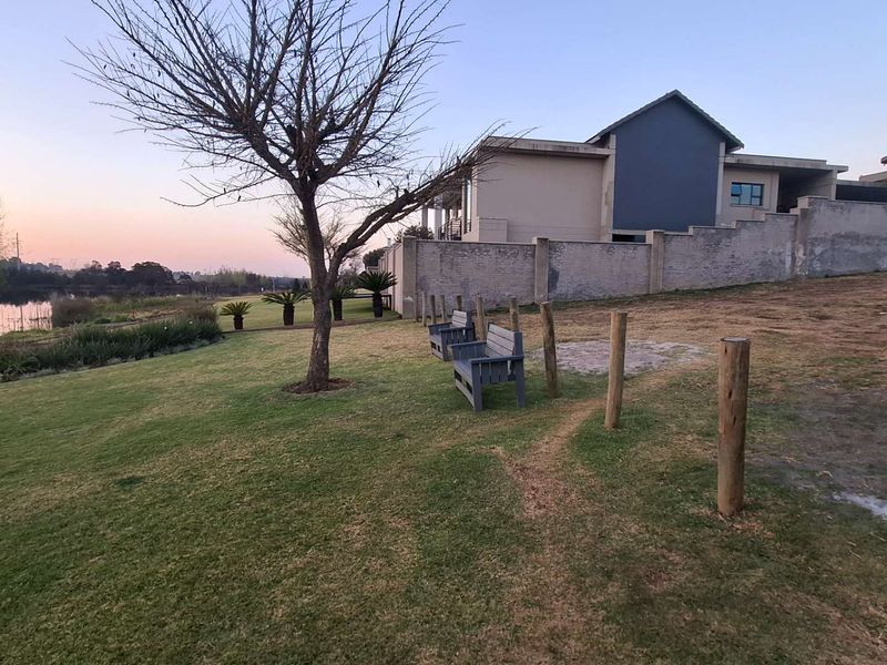 A well-maintained garden area featuring a lawn, timber bollards, and a boundary wall, overlooking a tranquil waterfront setting.