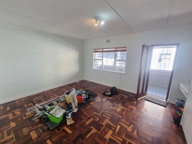 A vacant living room featuring traditional parquet flooring, a ceiling light fixture, and direct access to an exterior balcony through a timber door.
