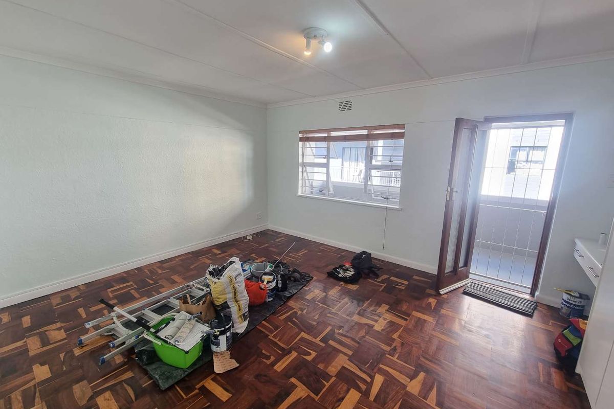 A vacant living room featuring traditional parquet flooring, a ceiling light fixture, and direct access to an exterior balcony through a timber door.