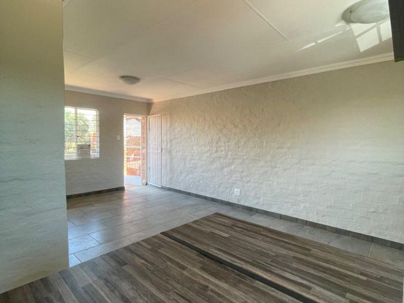 An open-plan living area featuring a combination of laminate and tiled flooring, neutral textured walls, and direct access to an exterior security gate.