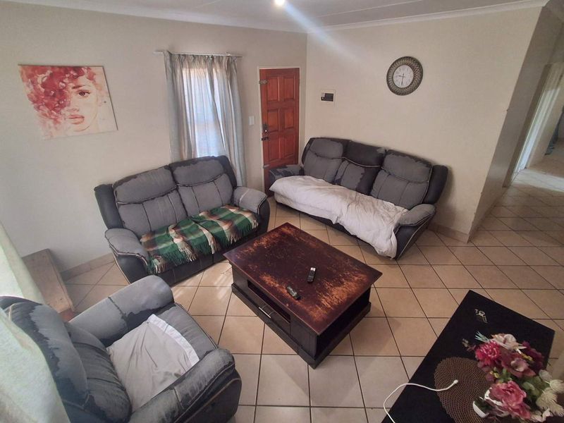 A living room featuring tiled flooring and a wooden entrance door, providing a functional and neutral space for relaxation.