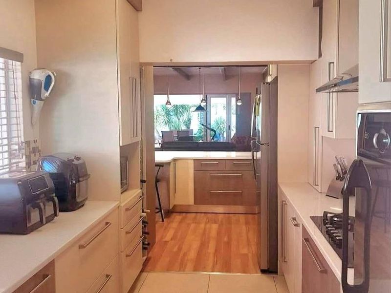 A functional galley-style kitchen featuring modern cabinetry, stone countertops, built-in oven, and gas hob, with a view through to the adjacent living area.