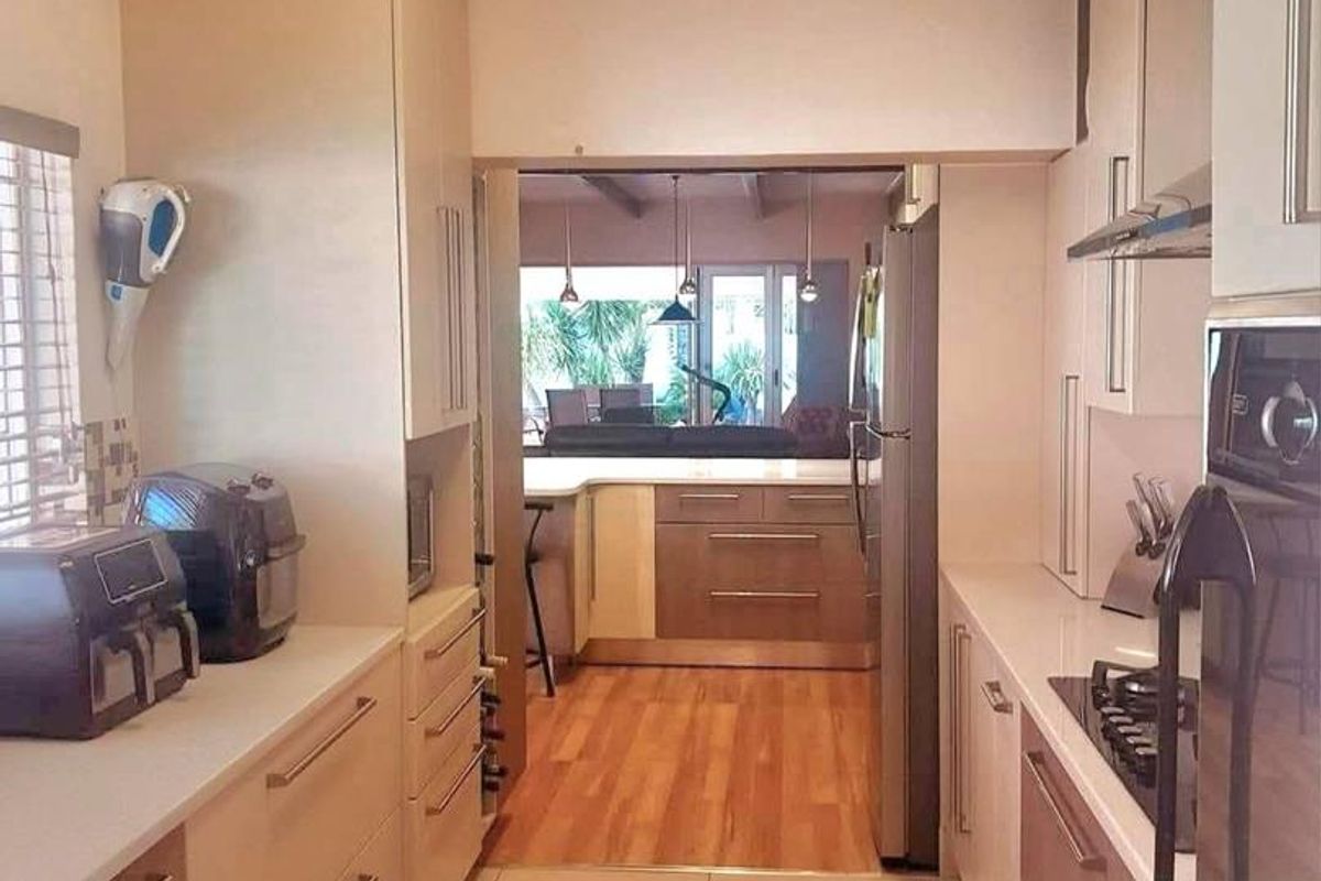 A functional galley-style kitchen featuring modern cabinetry, stone countertops, built-in oven, and gas hob, with a view through to the adjacent living area.